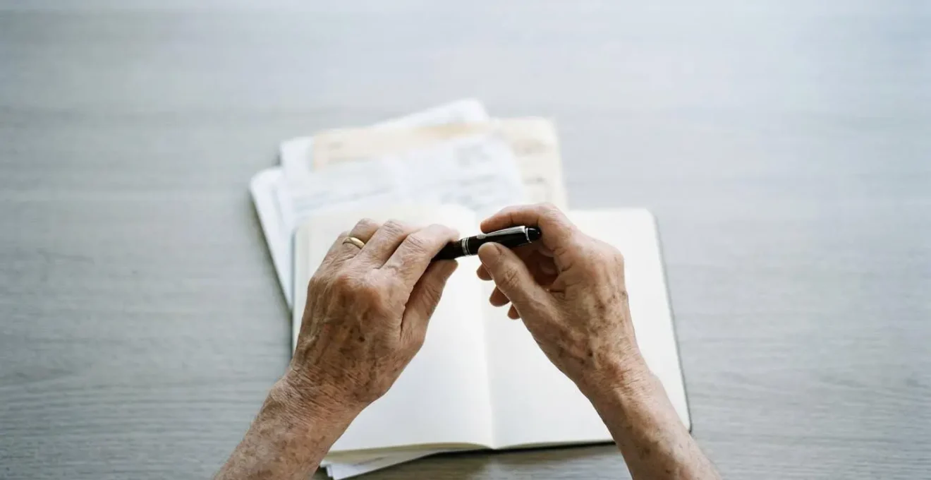 Mains de personne âgée tenant un stylo au-dessus de documents flous