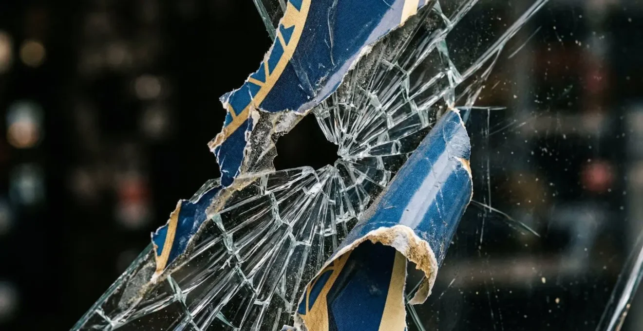 Gros plan sur une vitrine commerciale endommagée montrant des fragments de verre et des décalcomanies partiellement détachés